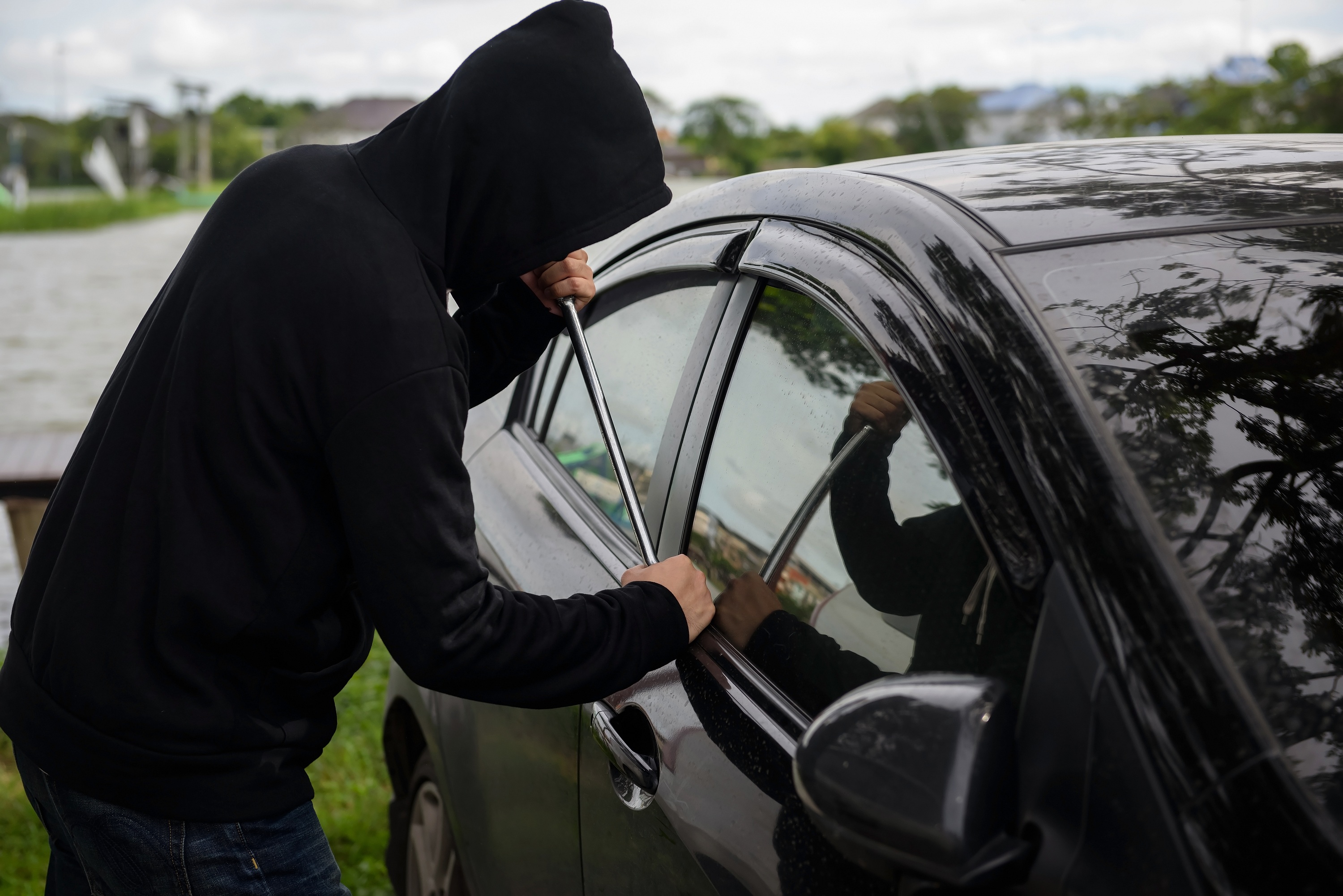 Robber man in black hoodie jacket and mask using a crowbar on his hand to break lock and steal a vehicle. Car thief or theft for insurance concept