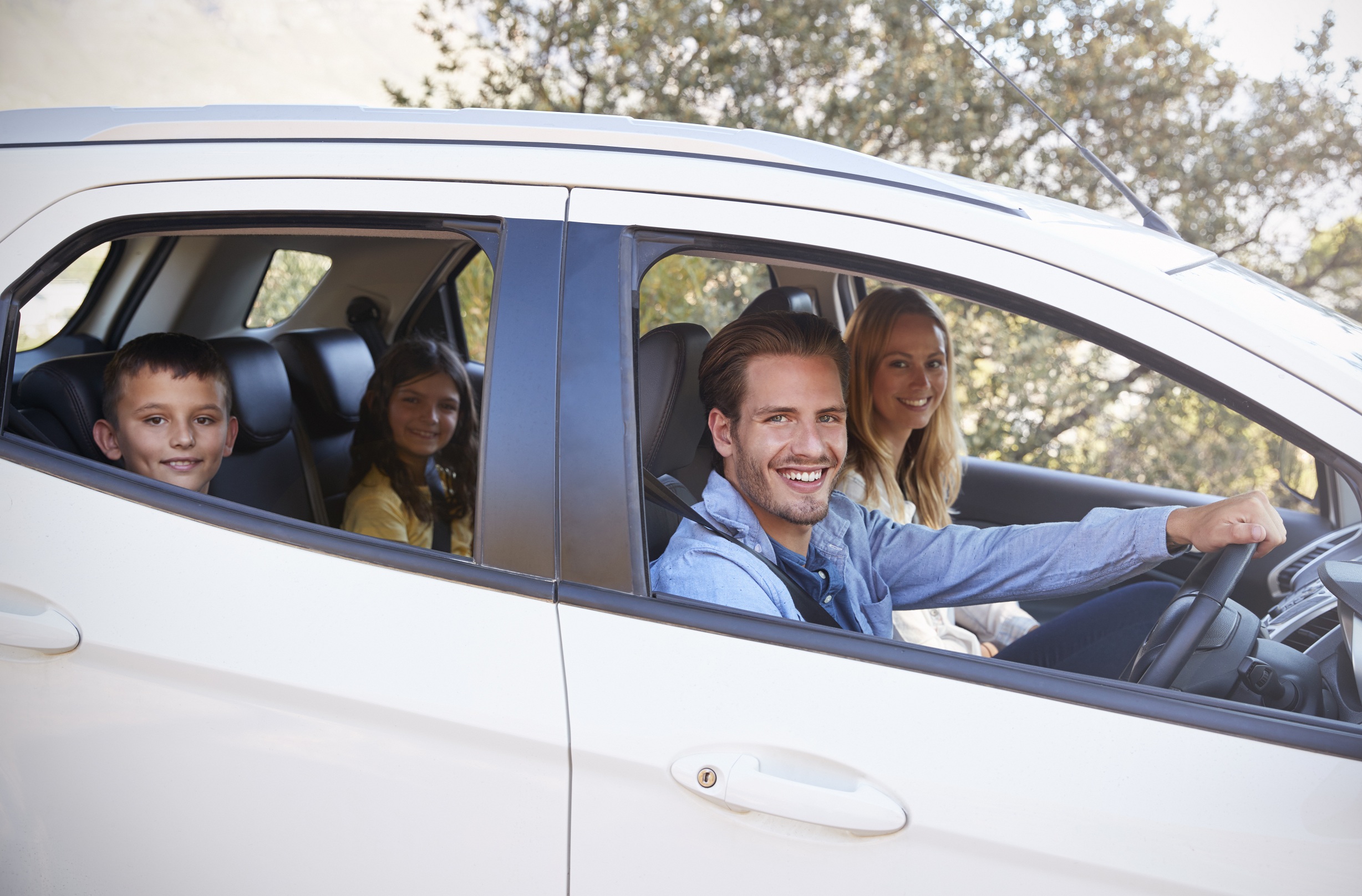 Happy young family driving in their car looking to camera